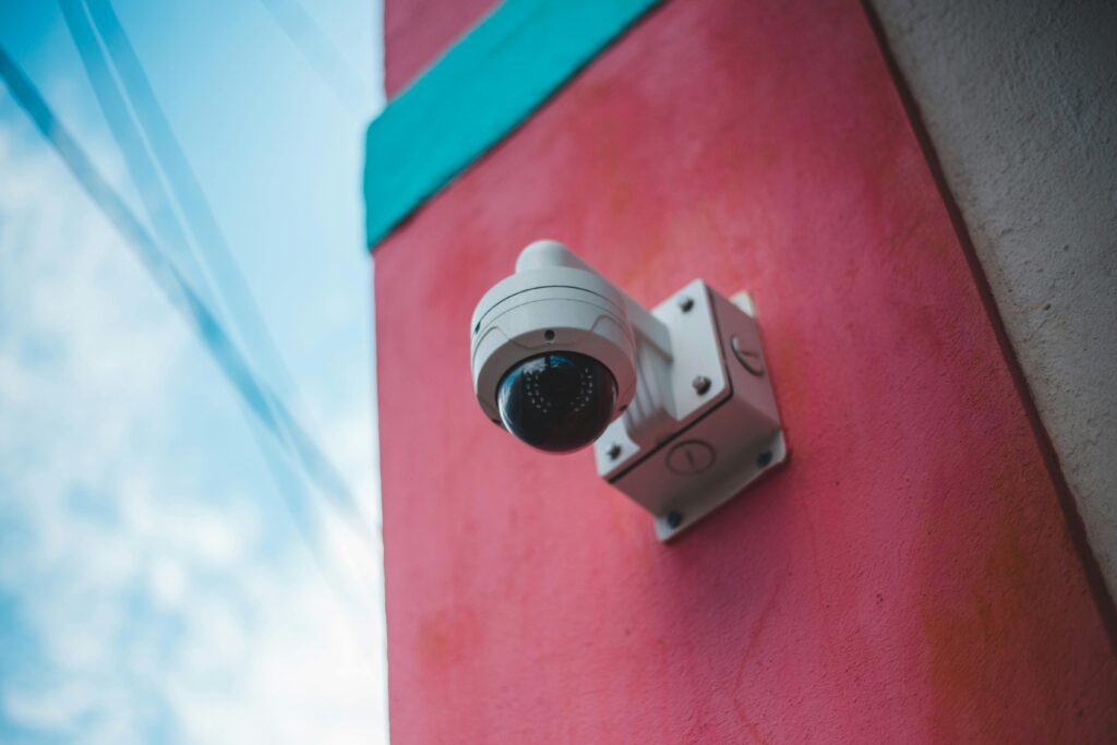 pexels-photo-7635126-7635126 A surveillance camera mounted on a vibrant pink and teal wall outdoors.